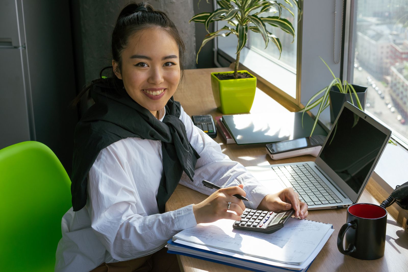 A smiling bookkeeper at a desk with a calculator and laptop