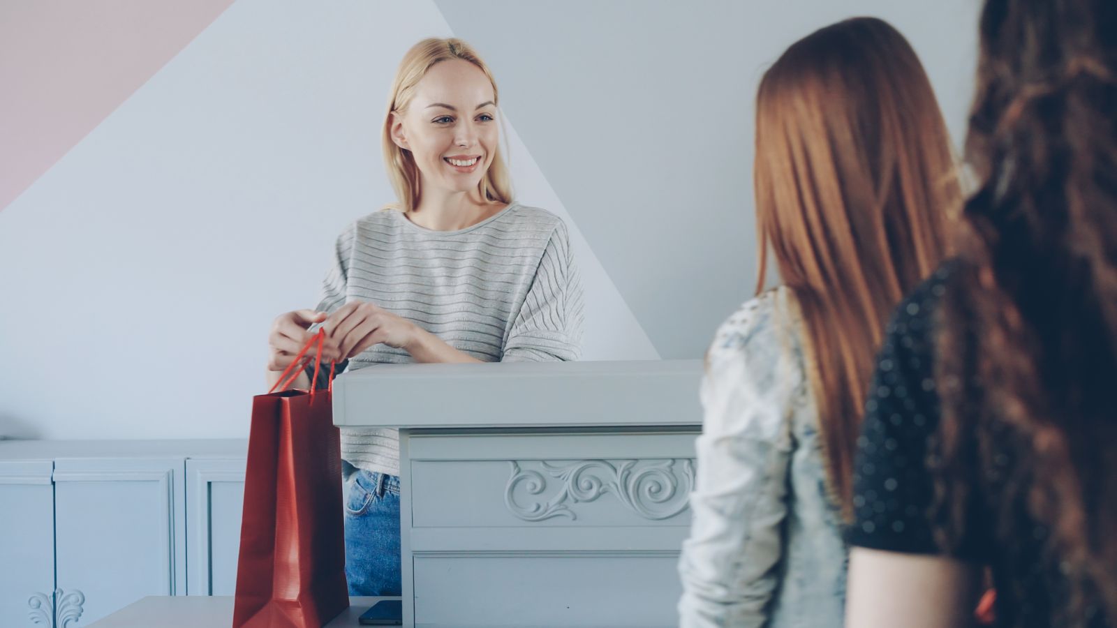 A cheerful cashier handing a shopping bag to two customers