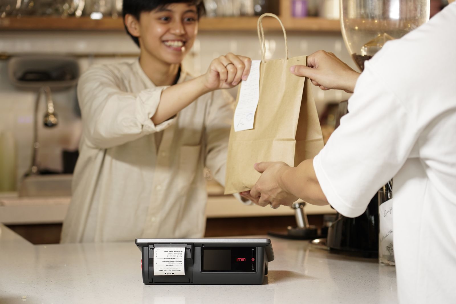 A smiling cashier handing a paper bag to a customer across the counter