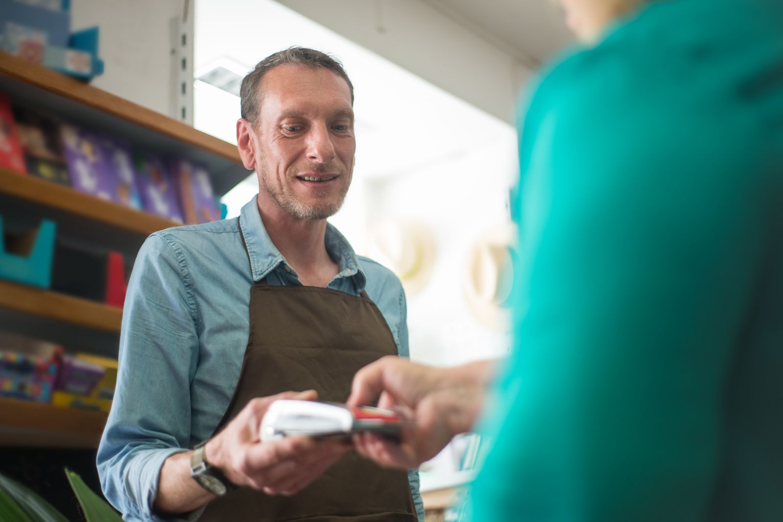 A store clerk in an apron smiling as he takes a customer card on the terminal