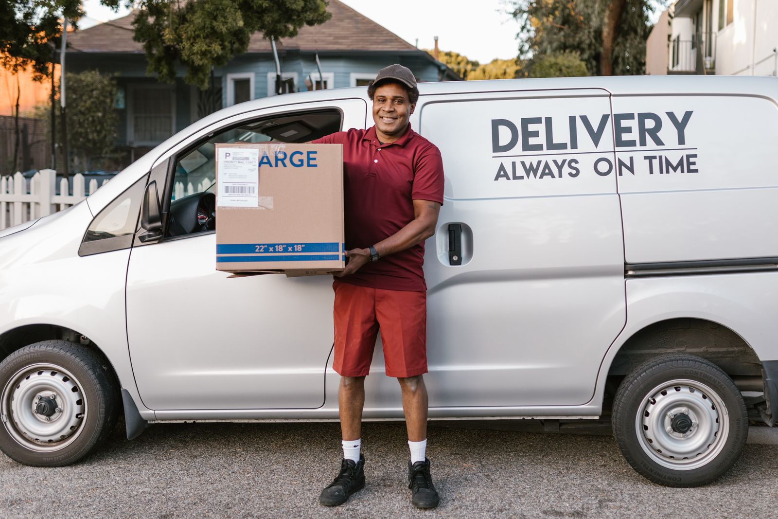 A smiling delivery driver carrying a package beside his van