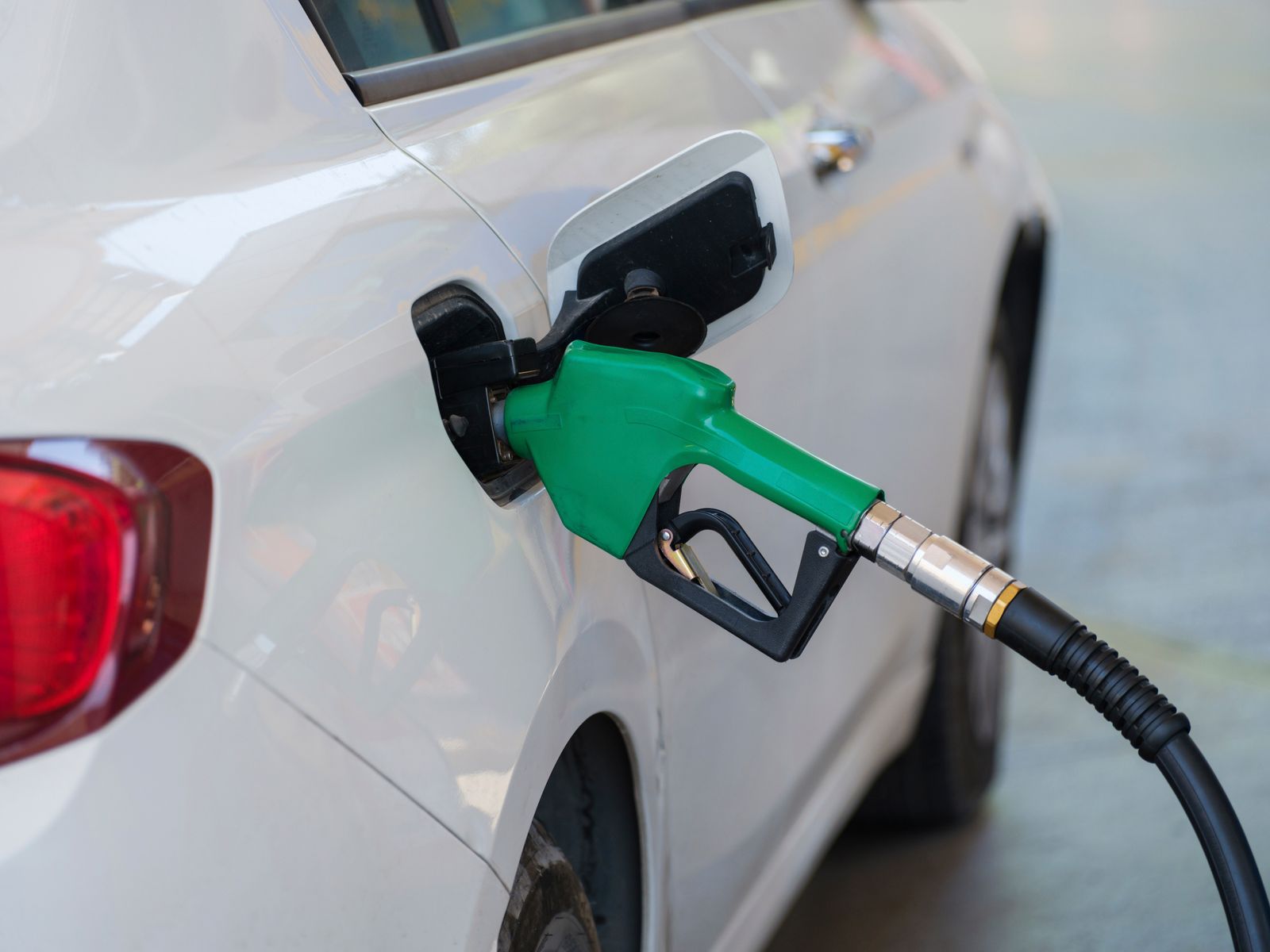 A green fuel nozzle refuelling a white car at a gas station pump