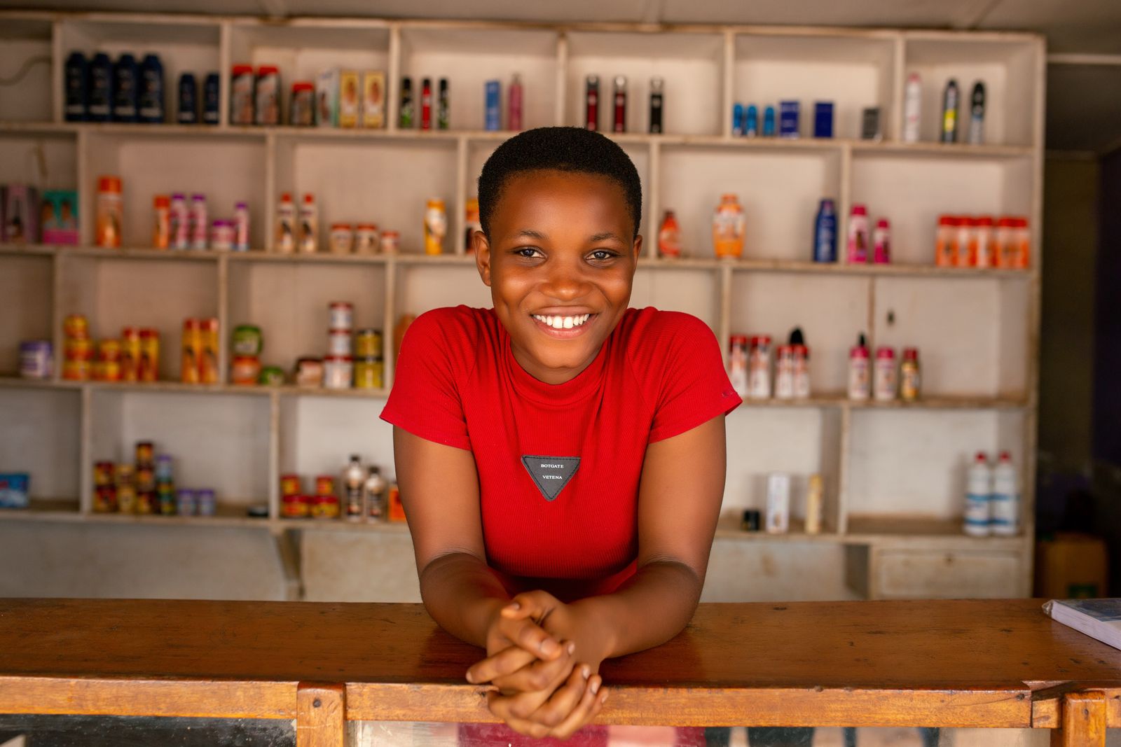 A cheerful store owner leaning on the counter in front of stocked shelves
