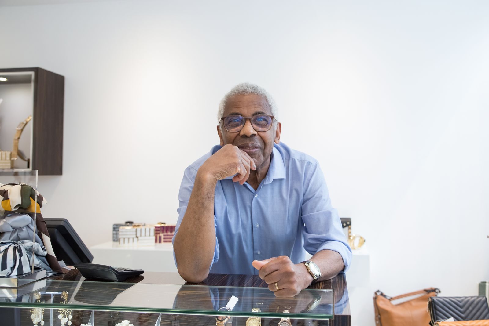 A smiling shop owner leaning on the glass counter of his store