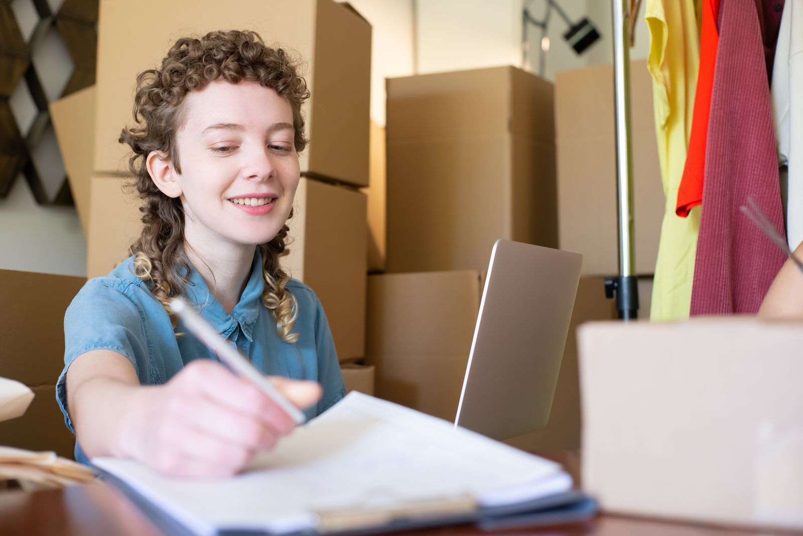 A smiling young owner at a laptop surrounded by shipping boxes
