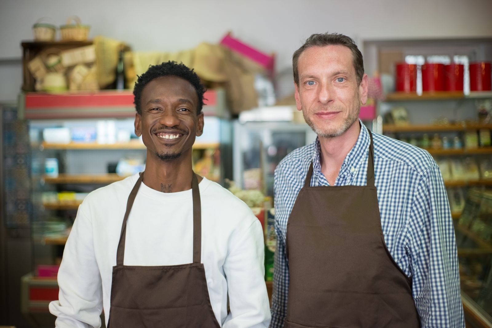 Two store employees in brown aprons standing together in a small grocery store