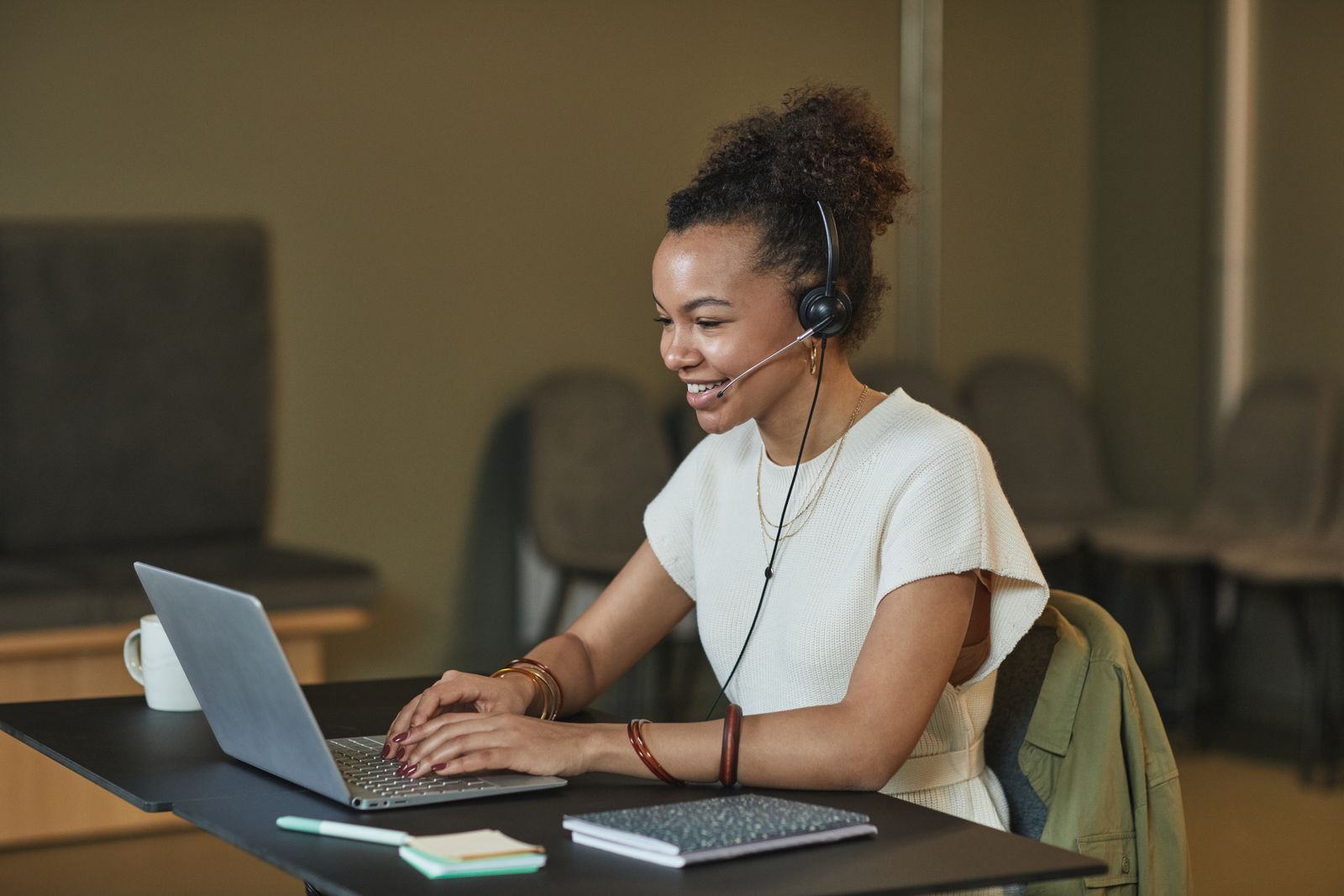 A smiling agent wearing a headset working at a laptop