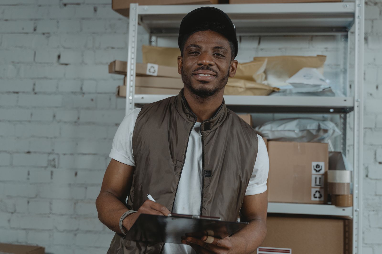 A smiling warehouse employee with a clipboard among shelves of packages